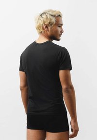 Czarny t-shirt z krótkim rękawem wykonany z bawełny, z klasycznym okrągłym dekoltem i dopasowanym krojem, noszony z czarnymi szortami.