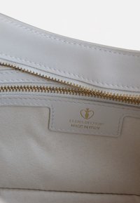 Innenseite einer weißen Ledertasche mit goldenen Reißverschluss und Nähten. Enthält ein Etikett mit der Aufschrift "ELENA DI GIORDI MADE IN ITALY" auf einem passenden Stoff.