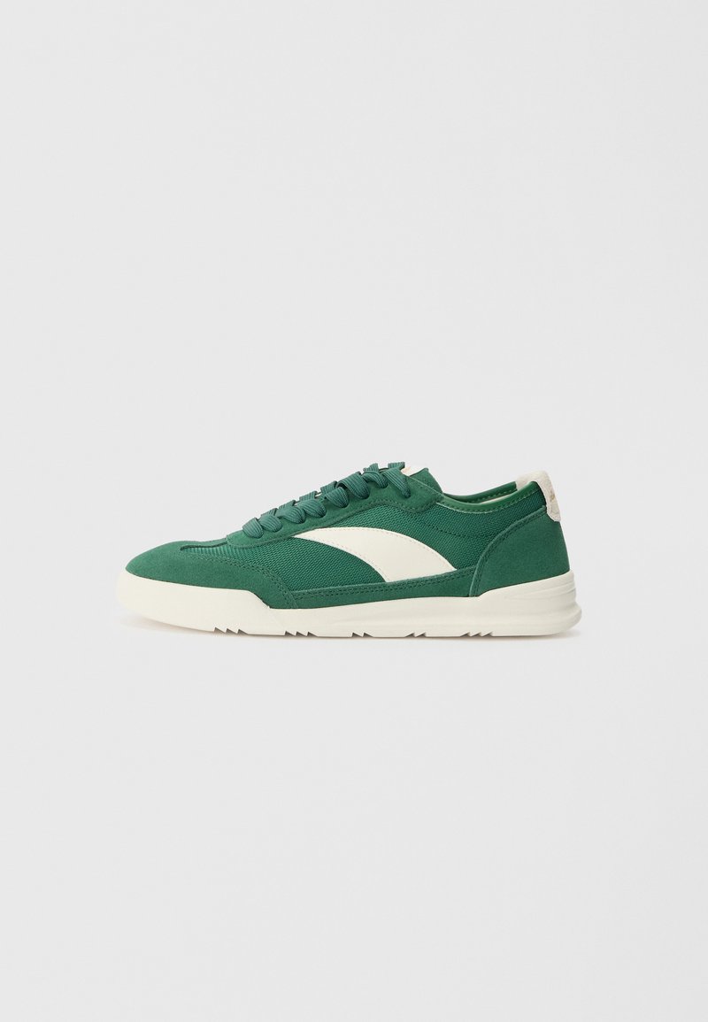 Zöld vászon sneaker, krémszínű csíkozással, kerek fűzős, és enyhén emelt, texturált gumitalppal.