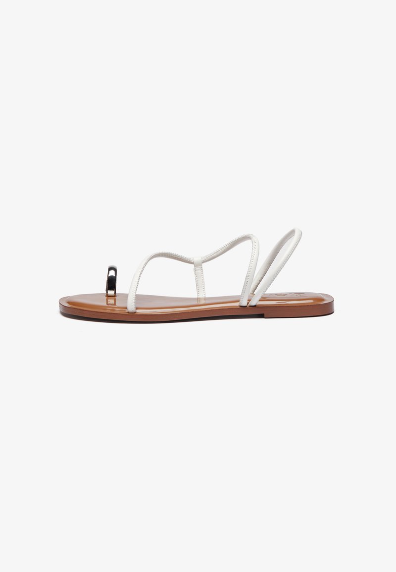 Hvide læder flade sandaler med tynde stropper, brun sål og en sort detalje ved tæerne. Slank, minimalistisk design med en glat tekstur.