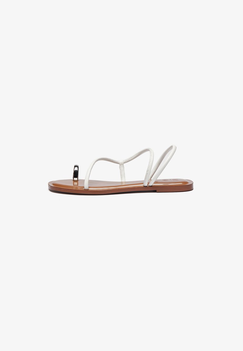 White leather flat sandals with thin straps, brown sole, and a black accent at the toe. Slim, minimalistic design with a smooth texture.