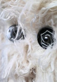 Pluche dier met fuzzy witte vachttextuur, met grote zwarte knopenogen met een hexagonale rand en witte draadaccenten.