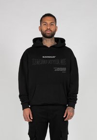 Svart hettegenser med frontlomme, stort grafisk tekst "LEGENDS NEVER DIE" og merke-logo på brystet, laget av myk stoff.