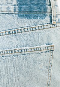 Tissu en denim bleu clair avec un ourlet non fini, des bords effilochés et des nuances variées avec un motif délavé.