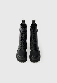 Melnas ādas auklu zābaki līdz potītēm ar biezām gumijas zolēm, polsterētu apkakli un vilkšanas cilpu vieglai uzvilkšanai. Iezīmētas ar metāliskām acīm un šuvēm.