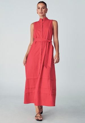 Rdeča maksi obleka z mandarin ovratnikom, brez rokavov, sprednjim zapiranjem na gumb in vezi okoli pasu. Horizontalni detajli šivov.
