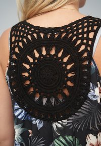 Sort macramédetalje med cirkulært mønster bagpå, der viser en indviklet vævning. Blomstermønstret stof i blå, grønne og hvide farver.