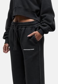 Zwarte cropped sweatshirt en bijpassende sweatpants van zachte stof, met een elastische tailleband en de tekst "GOODFORNOTHING" op de broek.