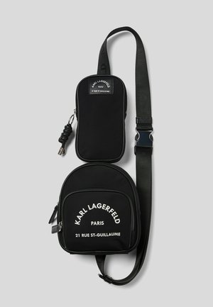 Borsa a tracolla nera in tela con scomparto principale arrotondato e tasca rettangolare. Presenta lettere bianche e dettagli con zip.