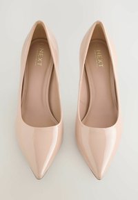 Nude pumps van lakleer met een puntige neus en een glanzende afwerking, met een gladde textuur en minimalistisch ontwerp. Merklabel zichtbaar aan de binnenzijde.