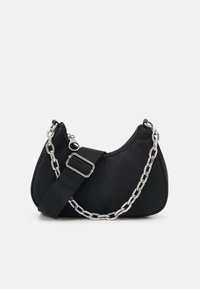Sac à épaule en tissu noir avec une silhouette courbée, doté d'un accent en chaîne argentée et d'une bandoulière ajustable avec une boucle. Fermeture zippée en haut.
