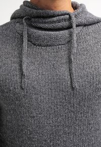 Grau gestrickter Pullover mit einem hohen, umgeschlagenen Kragen und Kordelzugakzenten. Verfügt über ein strukturiertes Muster und gerippte Bündchen.