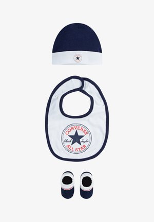 Gorro de malha azul-marinho, babete branco com logótipo em vermelho e azul, e botinhas azul-marinho com detalhes brancos. Material em algodão, formas redondas, acessórios para crianças pequenas.