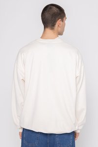 Sudadera de gran tamaño color crema con cuello redondo, hombros caídos y puños de canalé. Textura suave; diseño simple y sin adornos.