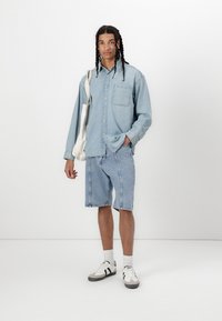 Cămașă din denim albastru deschis cu nasturi, șorturi din denim assortate, șosete albe și adidași gri cu dungi negre. Tote din pânză purtat pe umăr.