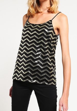 Vrouw draagt een zwart en goudkleurig zigzag pailletten mouwloos top met dunne bandjes en een zwarte broek.