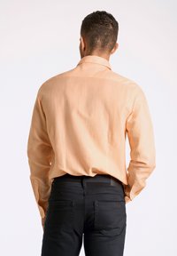 Helles Pfirsichfarbenes Langarmhemd mit klassischem Kragen, knöpfbaren Manschetten und lockerer Passform, kombiniert mit dunklen schwarzen Jeans.
