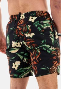 Costume da bagno neri con un vivace motivo floreale tropicale che presenta foglie verdi e fiori bianchi. Vita elasticizzata con tasca sul retro.