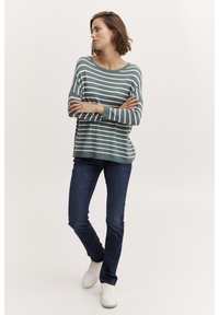 Gestreiftes Strickoberteil in Türkis und Weiß, mit lässiger Passform, langen Ärmeln und weitem Ausschnitt, kombiniert mit dunkelblauen Jeans und weißen Sneakers.