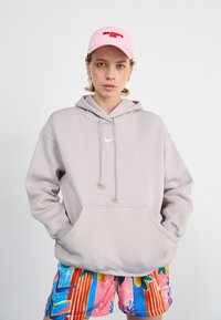 Ljusgrå Nike-hoodie med känguruficka, dragsko och liten vit logotyp. Matchad med färgglada, mönstrade shorts med blommönster.