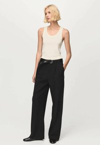 Top de tirantes color beige claro con escote redondeado, combinado con pantalones negros de pierna ancha y cintura alta, y un cinturón negro con hebilla redonda.