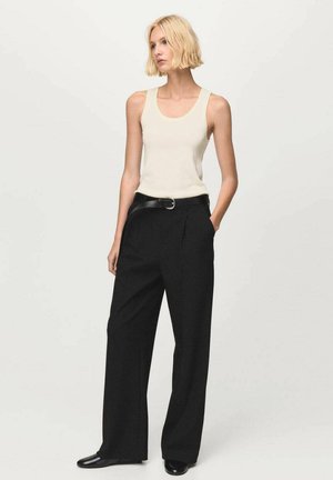 Top de tirantes color beige claro con escote redondeado, combinado con pantalones negros de pierna ancha y cintura alta, y un cinturón negro con hebilla redonda.