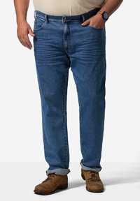 Jeans de mezclilla azul con un ligero desgastado, corte recto, cinco bolsillos y dobladillos enrollados, combinados con zapatos marrones de cordones.