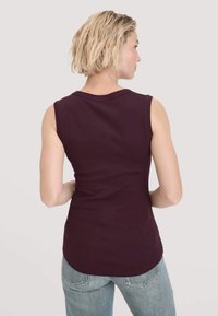 Ärmelloses, enges Oberteil aus dunkelviolettem Stoff mit glatter Textur und abgerundetem Saum, kombiniert mit hellblauen Jeans.