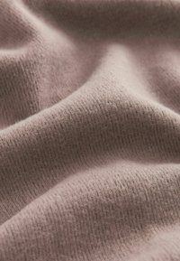 Blødt, struktureret stof i en dæmpet pink farve, med et fint ribbet mønster. Materialet fremstår varmt og hyggeligt, med subtil dybde i folderne.