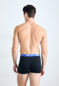 Boxer brevís negros de tela elástica, con una cinturilla azul con la marca Nike. Costura visible y aberturas en las piernas, diseño ajustado.