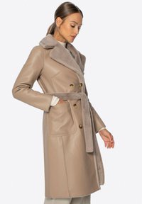 Beige Lederjacke mit weitem Pelzkragen, doppelter Knopfleiste, zwei vorderen Taschen und einem passenden Stoffgürtel.