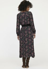 Langes Blumenkleid mit dunklem Hintergrund, das ein Muster aus pinken und grünen Blumen zeigt. Taillierter Gürtel und Ballonärmel. Weicher Stoff.