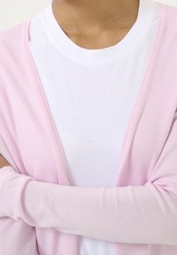 Cárdigan de color rosa claro con mangas largas, diseño de frente abierto y textura ligera, superpuesto a una camiseta blanca sencilla.