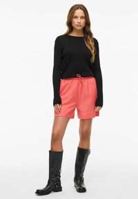 Sort ribbet striktrøje, koralfarvede shorts med snøre og knæhøje sorte støvler. Stoffet ser blødt ud, med en afslappet pasform og et afslappet design.