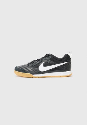Black athletic shoe with a textured upper, white Nike swoosh, and gum rubber outsole. Features laces and a snug fit design.