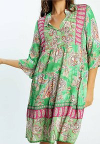 Vestido floral verde con cuello tipo polo, mangas tres cuartos y diseño en capas. Presenta acentos en rosa y patrones intrincados en toda la prenda.