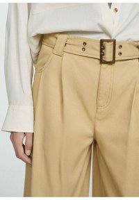 Beige hoog-taille broeken met een wijde pijp, voorzien van een vierkante metalen gesp en subtiele voorplooien. Glad, duurzaam stof.