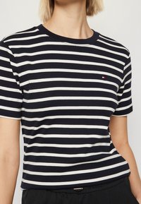 T-paita, jossa on meriaiheiset valkoiset raidat, pyöreä pääntie, lyhyet hihat ja pieni brändilogo rinnassa. Valmistettu pehmeästä, joustavasta materiaalista.