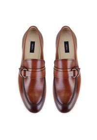 Bruine leren instappers met een afgeronde neus, decoratieve gesp en een witte rubberen zool; gladde textuur met minimale stikseldetails.