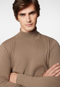 Brązowy sweter typu golf wyk wykonany z dzianiny; charakteryzuje się dopasowanym krojem, prążkowanym kołnierzem oraz długimi rękawami z dopasowanymi mankietami.