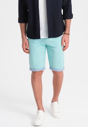 Shorts bleu clair avec revers, en coton, associés à une chemise bleu marine et des baskets blanches. Design épuré et simple.