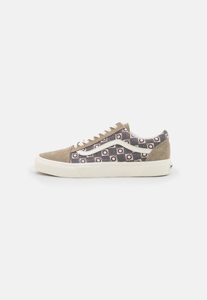 Zapatilla baja con puntera y talón de ante beige, laterales de tela con patrón geométrico en azul y crema, y suela de goma blanca.