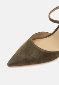 Chaussure femme en daim vert olive à bout pointu avec bride à la cheville et doublure intérieure beige sur fond blanc.