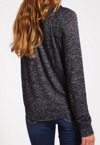 Långärmad, mörkgrå melerad topp med rund halsringning och avslappnad passform. Den har mjukt tyg och subtila sömnadsdetaljer.