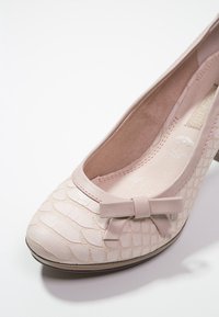 Escarpin rose clair avec motif texturé reptile, bout arrondi, talon bas, et nœud décoratif sur le dessus. Doublure intérieure lisse visible.