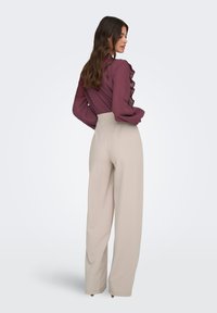 Μπλούζα μαρουν με υφή και βολάν, συνδυασμένη με μπεζ παντελόνι φαρδιάς γραμμής και ψηλή μέση. Λείο ύφασμα και άνετη εφαρμογή.