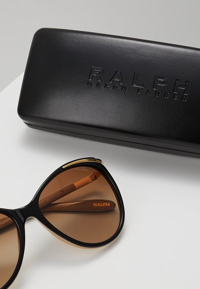 Černé sluneční brýle s hnědými skly ve velkém, kočičím tvaru. Součástí je černý kožený obal s vyraženým nápisem "RALPH RALPH LAUREN."