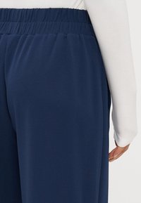 Navy blue, joustava kangas housut, joissa on elastinen vyötärö, sileä pinta ja rento istuvuus. Näkyvä sivusauman yksityiskohta.