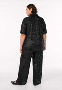 Conjunto negro de lentejuelas que presenta una blusa de manga corta con cuello y pantalones de pierna ancha, exhibiendo una superficie brillante y texturizada.