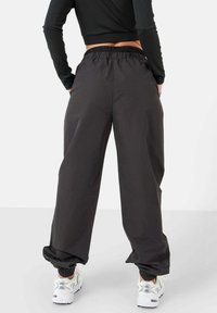 Pantalones anchos negros con cinturilla elástica y tobillos ceñidos, fabricados con un material suave, combinados con zapatillas deportivas blancas.